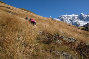 Snowy mountains Dzhangi-Tau and Shkhara with Khalde Glacier, with green mountainsides and silhouettes of wandering tourists in foreground. Greater Caucasus, Svaneti, GeorgiaSvaneti