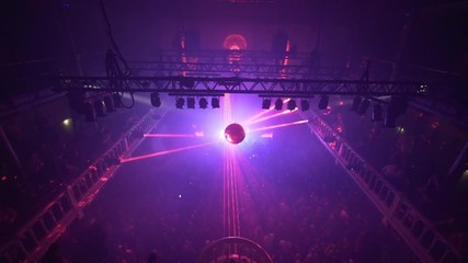 Red Lasers reflecting from disco ball above full dancefloor in nightclub disco club