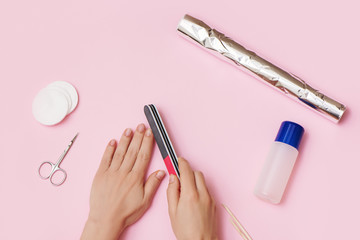 Woman hands removes nail polish on pink background.