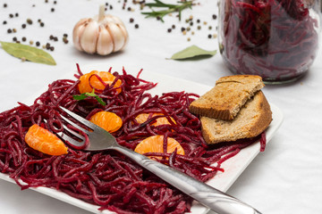 Two slices of mandarin on sliced fermented beets and fork in plate. Glass jar with beets. Garlic.