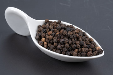 Whole black peppercorns in a white porcelain dish on a black background