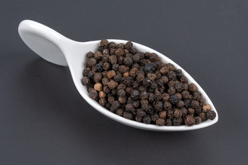 Whole black peppercorns in a white porcelain dish on a black background