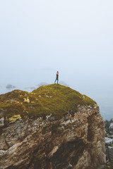 Obraz premium Woman standing alone on rocky cliff travel vacation adventure lifestyle outdoor isolation solitude depression concept foggy landscape seaside in Norway