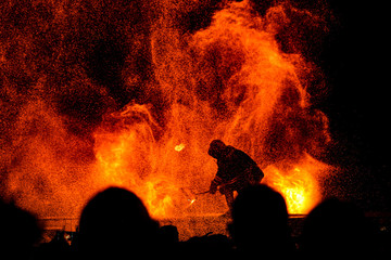 Silhouette of a firefighter fighting to contain a raging fire as a crowd looks on