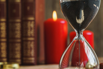 Hourglass and red burning candles close up on wooden desk