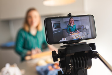 Young woman recording vlog at home in kitchen making croissants.