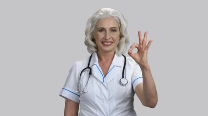 Old senior lady shows okay gesture. Grey isolated background.