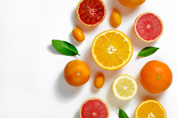 Fototapeta na wymiar Close up image of juicy organic whole and halved assorted citrus fruits, green leaves & visible core texture, isolated white background, copy space. Vitamin C loaded food concept. Top view, flat lay.
