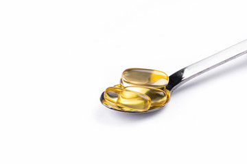 Pile of omega 3 fish liver oil capsules in spoon. Big golden translucent pills on isolated background. Healthy every day fatty acids nutritional supplement. Top view, flat lay, copy space, close up