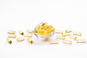 Bunch of omega 3 fish liver oil capsules in small glass bowl. Close up of golden translucent pills in pile. Healthy every day fatty acids nutritional supplement dosage. Top view, flat lay, copy space.