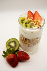 Oatmeal granola with nuts, fruit and yogurt. Strawberries and kiwis. Glass on a white background.