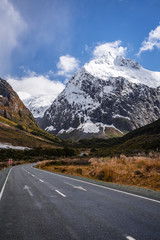 Naklejka premium Splendid image of the SH94 road towards Milford Sound surrounded by greenery with snow capped mountains in the background taken on a sunny winter day, New Zealand