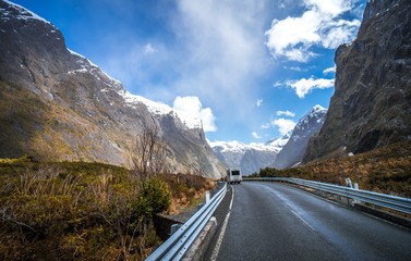 Splendid image of the SH94 road towards Milford Sound surrounded by greenery with snow capped mountains in the background taken on a sunny winter day, New Zealand