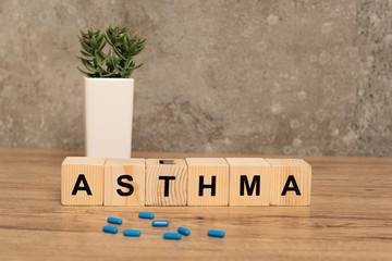 Selective focus of pills and wooden cubes with asthma lettering near plant on wooden table on grey background