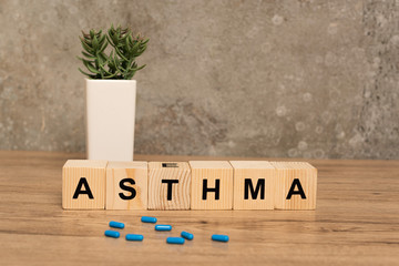 Selective focus of pills and wooden cubes with asthma lettering near plant on wooden table on grey...