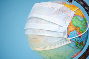 Globe with a medical mask close-up on a blue background with a copy of the space. concept of the coronavirus, infectious diseases