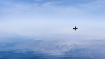 Mirror Surface Lake with a Lone fisherman on an inflatable boat and mice blue sky on background
