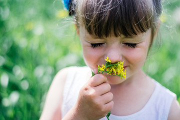 A little girl in  dress sniffing flowers in the garden.Portrait of smiling cute little girl outdoors.little girl sniffs flowers with her eyes closed.