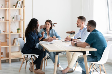 Concentrated multiethnic colleagues sit at desk in office discuss business idea together, focused diverse businesspeople gather at briefing brainstorm consider project at meeting, cooperation concept