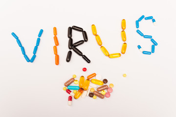 Top view of virus lettering and pile of pills on white background