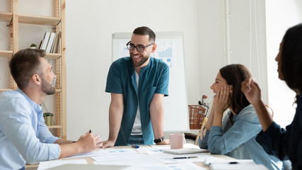 Smiling diverse businesspeople gather at desk in office have fun discussing ideas together, happy multiracial colleagues laugh talk brainstorming at team meeting or briefing, teamwork concept