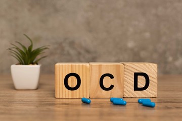 Selective focus of ocd letters on cubes near pills and plant on wooden surface on grey background