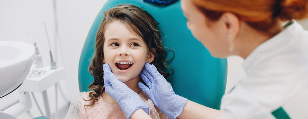Lovely kid smiling to the doctor while having a teeth surgery at the stomatology