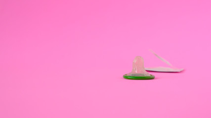Green condom on pink paper background with copy space for text. Reproductive health and safe sex...