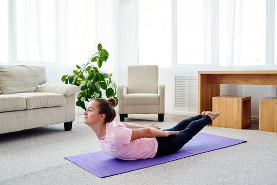 Portrait of young woman practicing yoga at home indoor, copy space. Girl stretching on mat, full length. Salabhasana (Locust pose). Wellness and healthy lifestyle