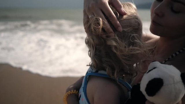 young mother hugs little curly girl on the sea beach in summer