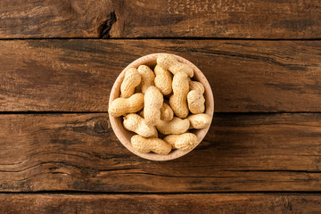 Overhead shot of peanuts in bowl on wooden table. Healthy snacks