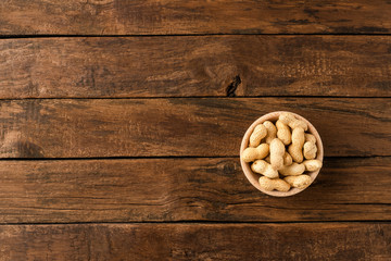 Tasty peanuts in bowl on wooden background with copyspace. Top view