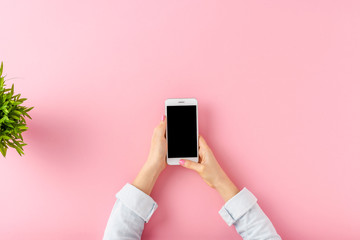 Young woman using mobile phone over pink table. Office desktop. Top view
