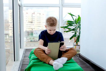 Child boy reads an e-book on a tablet and watches cartoons. Isolation from the outside world. World Quarantine, Coronovirus Pantemia, COVID-19. Close-up. The child is sitting on the balcony. To stay