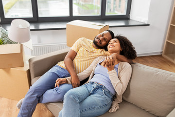 moving, repair and real estate concept - happy african american couple with cardboard boxes sitting...