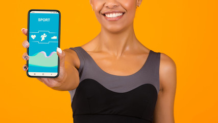Sporty African American woman showing mobile phone with fitness tracker app on yellow background,...