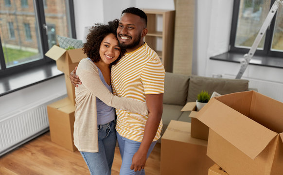 moving, repair and real estate concept - happy african american couple with cardboard boxes hugging at new home