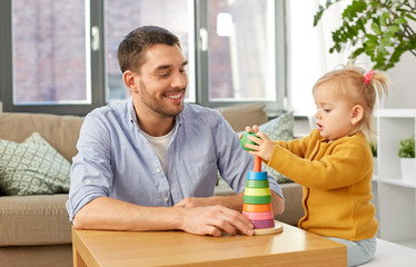 family, fatherhood and people concept - happy father and little baby daughter playing with pyramid toy at home