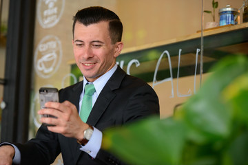 Happy young businessman using phone at the coffee shop outdoors