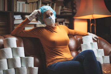 Woman with protective antiviral mask and a reserve of toilet paper waiting anxious in home...