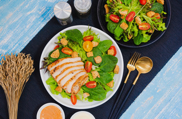 Couple bowl of healthy green vegetable salad on top with tomatos and biscuits. Side dish with salt pepper bottle, white cream and thousand island salad dressing