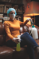 Woman with protective antiviral mask, chemical decontamination sprayer bottle in home isolation.