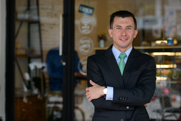 Happy young handsome businessman with arms crossed at the coffee shop outdoors