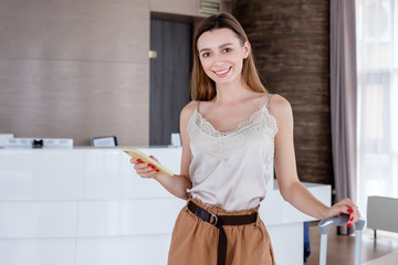 Portrait of a charming smiling girl with a smartphone and a suitcase orders a car in taxi service app while visiting hotels after a long vacation. Concept of good holiday experiences