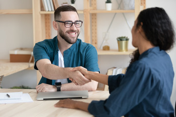 Fototapeta premium Smiling Caucasian male employer shake hand greeting get acquainted with female job candidate at office meeting, happy man recruiter handshake congratulate with promotion woman worker at briefing