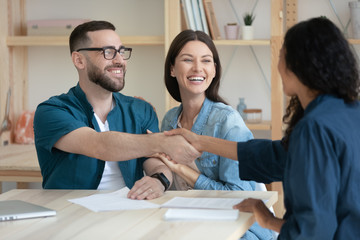 Overjoyed young couple shake hand greeting getting acquainted with marriage consultant, excited husband and wife handshake female real estate agent or broker, close deal at meeting in office