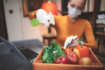 Woman with protective medical mask spraying sterilizing chemical on the food ordered from internet...