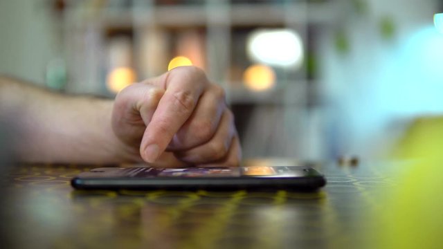Close-up, the phone is on the table, the guy will scroll the news feed. On a blurry background lights are on.
