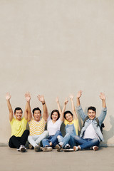 Group of happy excited young Asian people sitting at the wall and raising arms