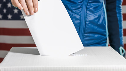 Woman voting and casting ballot in a box at flag of USA.